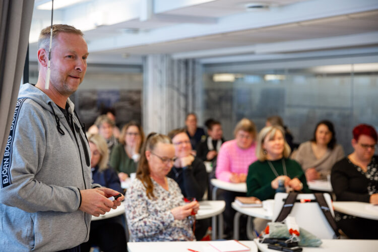 Opettaja salin edessä, aikuisopiskelijat. 